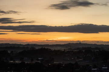Fototapeta premium Morning view at morning sunrise, clouds in orange crimson colors. Silhouettes of houses roofs, trees, and a monastery on the hill. Colorful scenery skyline background.