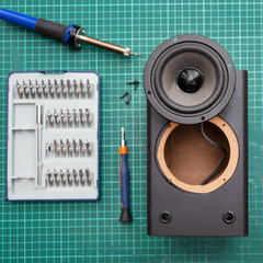 Audio speaker repair concept. Square photo. Broken audio speaker and repair tools in workshop. Flat lay.