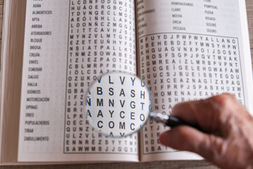 hand of an elderly woman holding a magnifying glass over a word search crossword puzzle