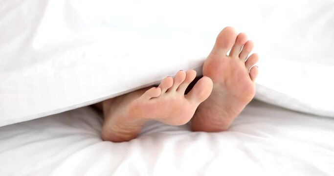 Closeup of woman legs under white blanket on bed