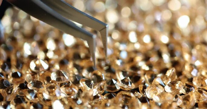 Diamond is clamped with pliers on table placed lot of diamonds
