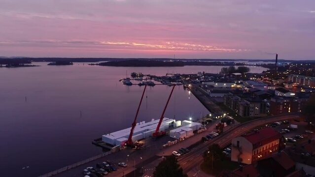 The harbor of the city of V&auml;stervik in Sweden. Calm sea with cargo ship unloading cargo in containers using cranes. Panorama of the port in the evening with pink clouds