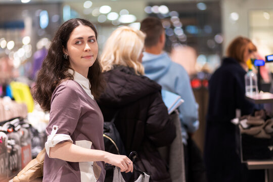 Portrait of young Caucasian smiling woman looking back and standing in store queue to pay for purchase. Concept of shopping and Black friday sale