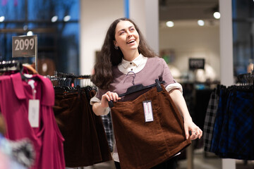 Shopping in secondhand. Happy smiling young Caucasian woman find best skirt. Concept of thrift store and sale