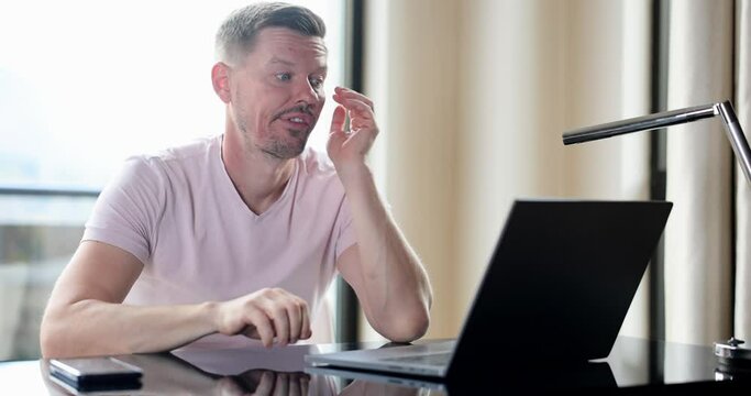 Bored man checking online laptop content sitting on table at home
