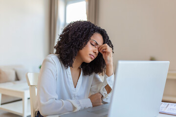 Fototapeta na wymiar Exhausted businesswoman having a headache in home office. African American creative woman working at office desk feeling tired. Stressed business woman feeling eye pain while overworking