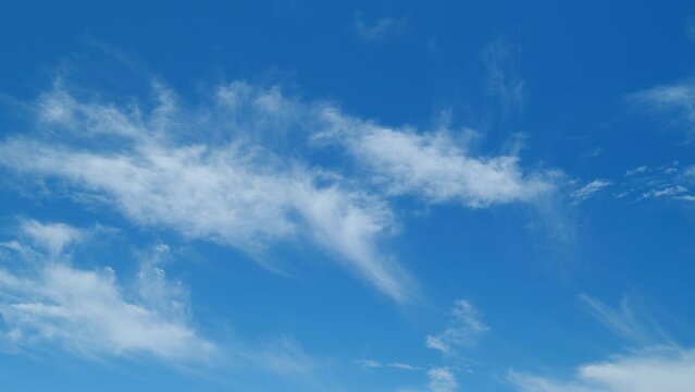 Blue clear sky with white cirrus spindrift clouds background. Light white cirrus clouds in blue sky on a summer day. Time lapse.