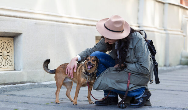 happy hipster woman playing with her dog on the street. stylish girl with funny dog resting, hugging and having fun, cute moments. space for text