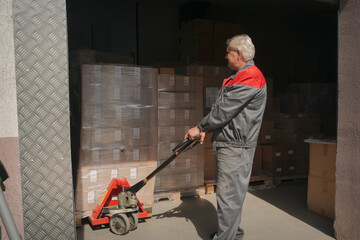 A loader rolls a trolley in a warehouse among many boxes. High quality photo.