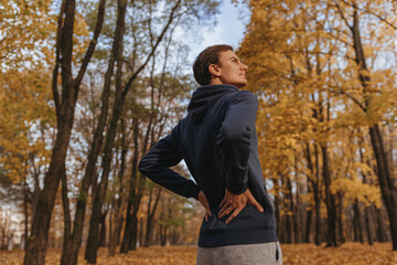 From below of fit male athlete stretching back and warming up during outdoor training in fall park...