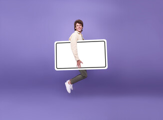 Happy young man jumping in the air with raised showing blank screen smartphone mobile isolated on purple background.