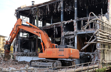Heavy orange excavator demolishes an abandoned industrial site for the urban redevelopment.