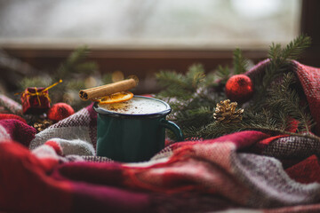 A mug of hot drink on a red checkered blanket. New Year and Christmas decorations. New Year and Christmas mood. Warm and cozy Christmas atmosphere. Close-up of a warm winter drink.