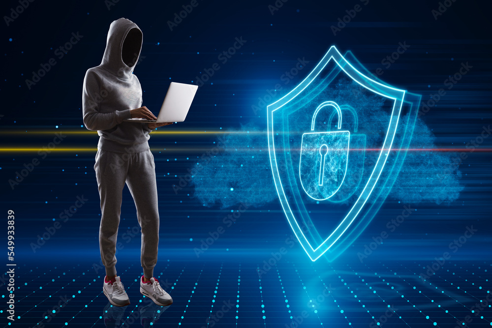 Aufkleber Hacker in hoodie standing and using laptop with glowing shield hologram on blurry background. Secure, protection, hacking, malware, safety and web security concept.