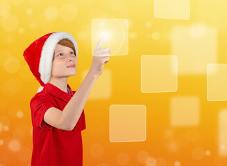 A cute boy in a Santa hat touching digital screen interface. Press on the golden gift icon. Modern technology choose your Christmas and new year present. Holiday online shopping.