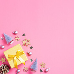 Square Christmas golden gift box with mini Christmas trees and baubles on pastel pink background