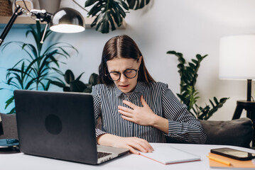 Close-up of young female in eyeglasses working at computer, difficulty breathing or pain in chest...