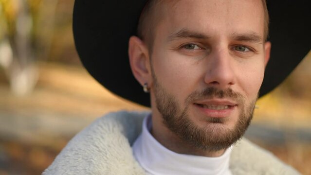 Close-up young man looking at camera taking off Covid-19 face mask exhaling. Handsome Caucasian LGBT guy posing on sunny day outdoors. Coronavirus pandemic and new normal lifestyle