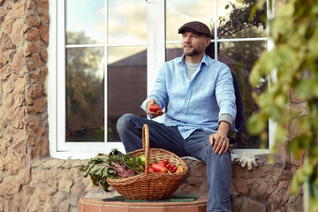 Close up of a mature male farmer is holding a basket with fresh harvested at the moment vegetables satisfied with his harvest