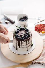 On the table is a delicious beautiful cake with berries for sale. Confectioner cuts off a piece. High quality photo