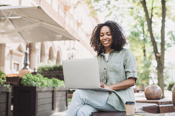 Young beautiful woman using laptop computer in a city. Smiling student girl typing laptop outdoor. Modern lifestyle, connection, online business, freelance concept