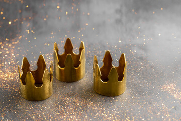 Epiphany  Day or Dia de Reyes Magos concept. Three gold crowns on black background with golden particles.