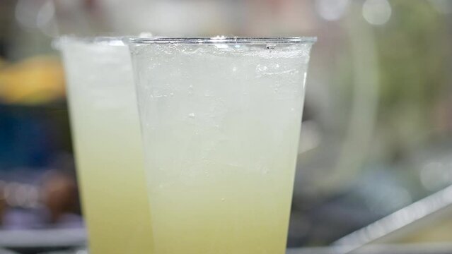 Close-up shot of unrecognized person making fresh, sparkling lemonade. Detailed view of caucasian female hand holding a cup of cold, delicious beverage. High quality 4k footage