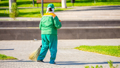 The janitor cleans the city street with a broom in the city. Street cleaning service. A worker sweeps the sidewalks in the park with a vine.