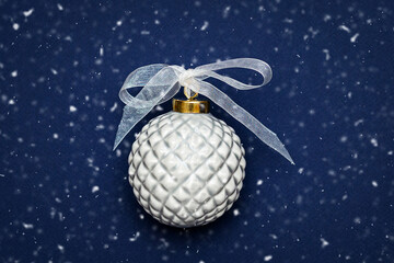 Porcelain Christmas bauble with a transparent ribbon on a dark blue background.Concept: Christmas and New Year holidays, greeting card.Top view. Copy space