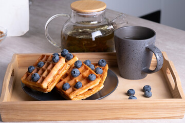 Waffles with blueberries. Cup of tea and teapot on a gray table.