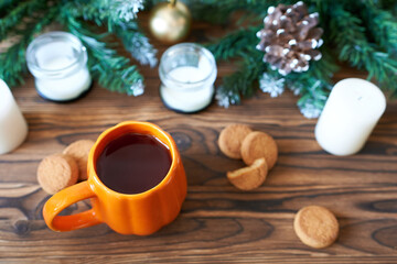 Orange tea mug on a wooden background with cookies and sprigs of Christmas tree. The concept is a New Year photo wallpaper.