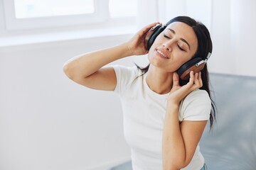 Woman listening to music on headphones sitting at home on a chair with her eyes closed, a smile and a good mood, a meditation to relieve stress