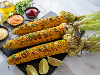 three heads of yellow corn grilled lemon lime spicy, white orange red sauce - 549949007