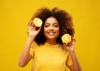 young afro american woman hold orange slices look amazed isolated on yellow color background.