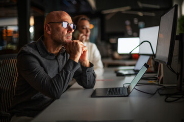 Tired businessman workingon computer  in office in late evening with him female colleague