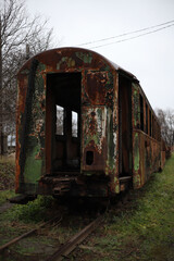 Fototapeta na wymiar an old rusty shabby train carriage without windows and doors with peeling green paint stands on the grass