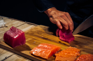 Close up of Chef cook hands chopping tuna fish for traditional Asian cuisine with Japanese knife. Professional Sushi chef cutting seafood japanese chefs are making tuna fish sashimi. dark tone