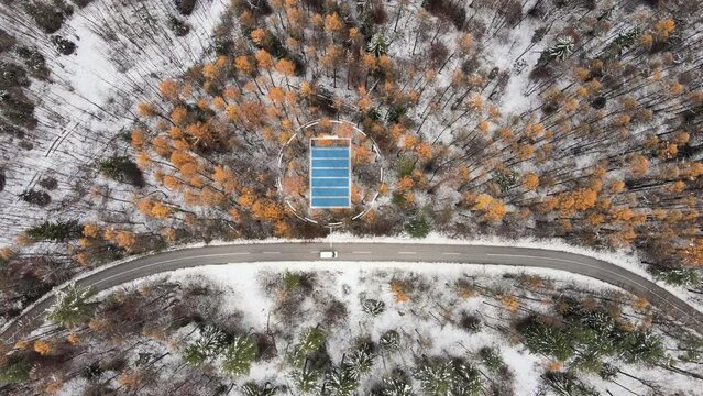 Aerial top down of white electric car driving through winter landscape with animation showing battery levels.