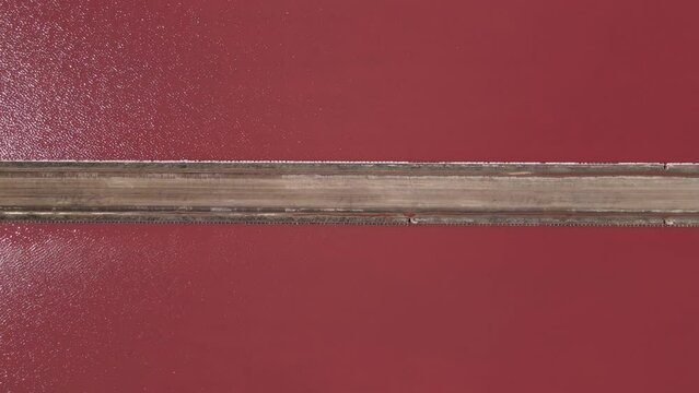 Bright pink lake view from above tracking a long and narrow walk way. 