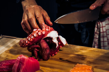 Close up of Chef cook hands chopping octopus for traditional Asian cuisine with Japanese knife....