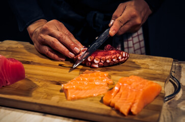 Close up of Chef cook hands chopping octopus for traditional Asian cuisine with Japanese knife. Professional Sushi chef cutting seafood japanese chefs are making octopus sashimi. Dark Tone