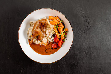 Dish of oatmeal with baked quail and vegetables on wooden background