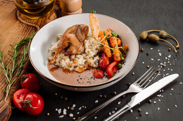 Dish of oatmeal with baked quail and vegetables on wooden background