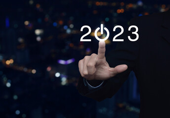 Businessman pressing 2023 start up business flat icon over blur colorful night light modern city...