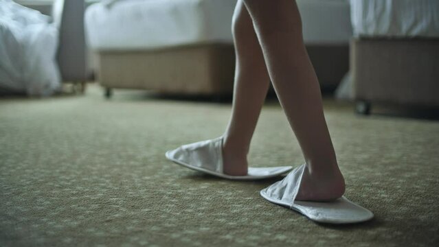Unknown little girl walks in a hotel room wearing too big hotel slippers for adult