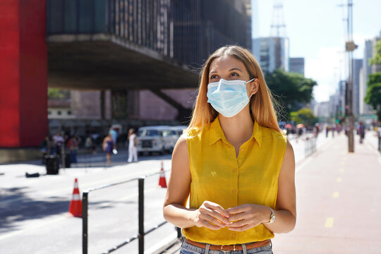 Beautiful young woman walking on Paulista Avenue wearing surgical mask in Sao Paulo, Brazil