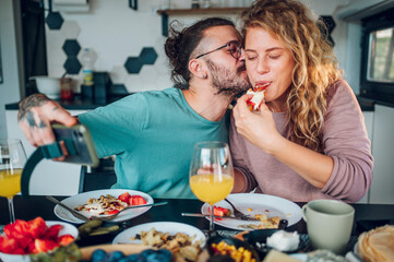 Couple eating breakfast together while sitting at table at home and taking selfie