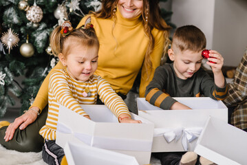 Happy family: mother, father and children, daughter and son, boy and girl unpack gifts near the Christmas tree and fireplace. Mom, dad hugs kids. New year concept. Merry Christmas. Close up.