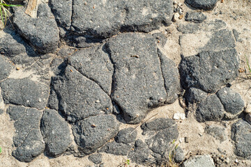 Background with old cracked asphalt covered with sand and gravel. Abandoned road with broken pavement.