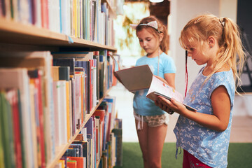 Two schoolgirls choosing books in school library. Primary school students learning from books. Children having fun in school club. Back to school